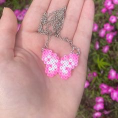 a hand holding a pink and white cross stitched butterfly necklace