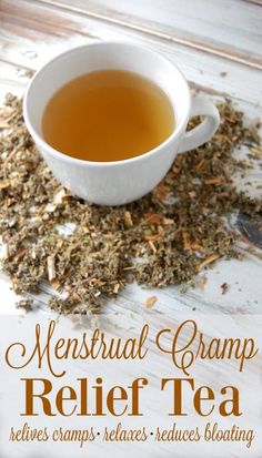 a cup of tea sitting on top of a table next to a spoon and some dried herbs