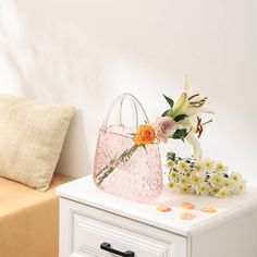 a pink purse sitting on top of a white table next to a flower vase and pillow