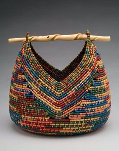 a multicolored woven purse hanging on a wooden stick in front of a gray background