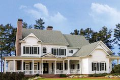 a large white house with lots of windows and porches on the front lawn, surrounded by greenery