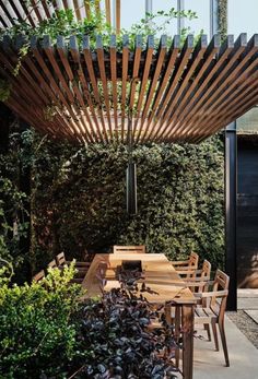 an outdoor dining area with wooden table and chairs under a pergolated trellis