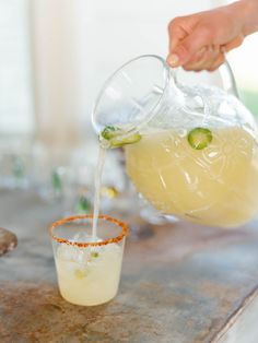 a person pours a drink into a glass with an orange garnish on the rim