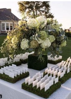 an arrangement of white flowers and greenery on top of a table in front of a house