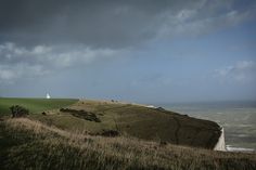 a lighthouse on top of a grassy hill with the ocean in the background and dark clouds overhead