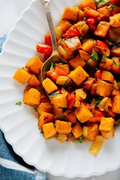 a white plate topped with cooked vegetables and a serving spoon on top of it next to a blue napkin