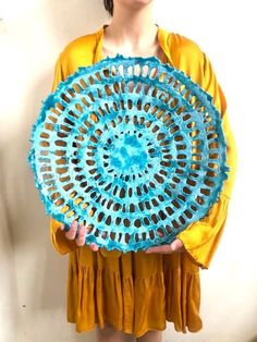 a woman holding a blue doily in front of her face and wearing a yellow top