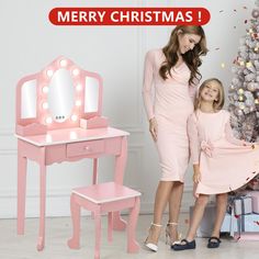 a mother and daughter standing in front of a pink dressing table with a lighted mirror