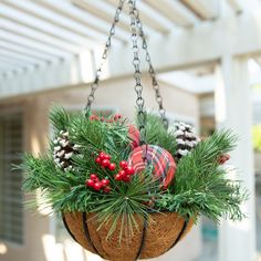 a hanging basket filled with pine cones, berries and other holiday decorations on a porch