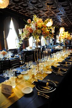 a long table is set up with black linens and gold place settings for an event