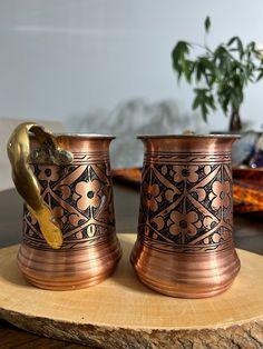 two metal cups sitting on top of a wooden table next to a potted plant