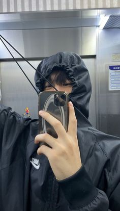 a person in a black jacket taking a selfie with a cell phone while wearing a raincoat