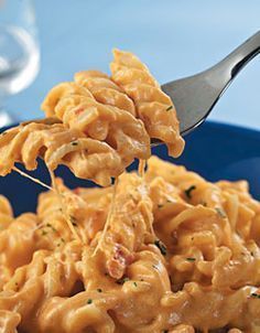 a fork full of macaroni and cheese being lifted from a blue plate with silverware