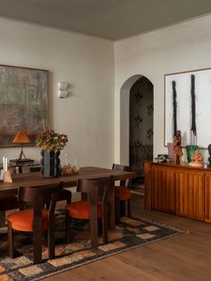 a dining room table with orange chairs and an art piece on the wall behind it