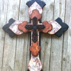 a cross made out of wood and decorated with floral designs on the side of a wooden fence