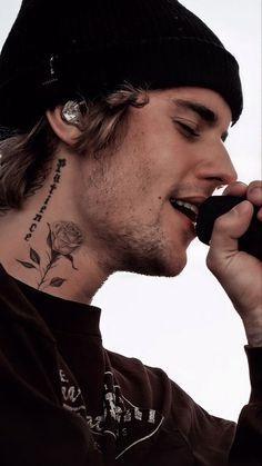 a man with a tattoo on his neck talking on a cell phone while wearing a beanie