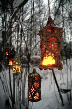 three lanterns hanging from branches in the snow