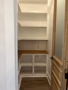 an empty walk in closet with white shelving and wood flooring on the side