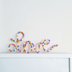 the word love spelled with colorful beads on top of a white shelf in front of a white wall