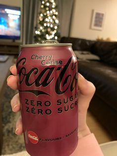 a person holding up a can of cherry cranberry soda in front of a christmas tree