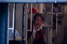 a man in a vest looking out from inside a train car, with his hand on the door handle