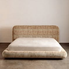 an upholstered bed with no sheets on it in a room that has concrete flooring and white walls