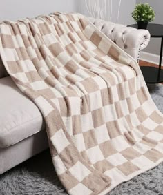 a couch covered in a checkered blanket next to a potted plant on the floor