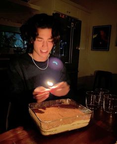 a woman holding a lit candle in front of a pan of food on a table