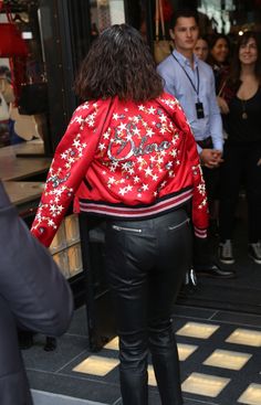 a woman in black leather pants and a red jacket is walking towards a store front