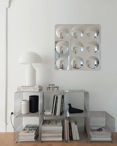 a mirrored wall mounted on the side of a white wall next to a shelf with books and magazines