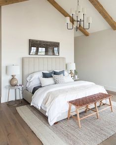 a bedroom with white walls, wood beams and an upholstered bed in the center