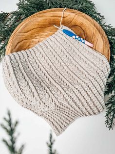 a knitted hat sitting on top of a wooden bowl next to evergreen needles and a blue toothbrush