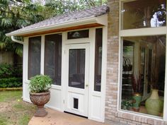 a white door and window in front of a brick house with potted plants on the porch