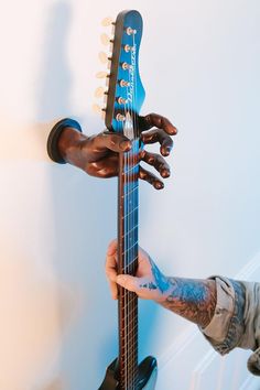 two hands holding an electric guitar in front of the camera and another hand reaching for it