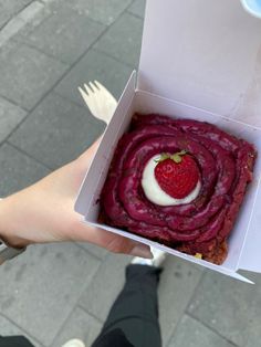 a person holding up a box with some food in it and a strawberry on top