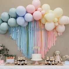 a table with cake, cupcakes and balloons in pastel colors on it