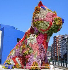 a large dog made out of flowers in front of a building with a blue sky