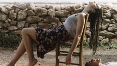 a woman laying on top of a wooden chair next to a man lying on the ground