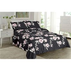 a black and white bed with pink flowers on the comforter is in front of a window