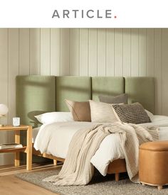 a bed with pillows and blankets on top of it next to a wooden table in front of a wall