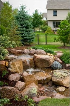 a garden with rocks and water running down the side of it, in front of a house