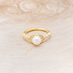 a gold ring with pearls on it sitting on top of a wooden table next to a piece of wood