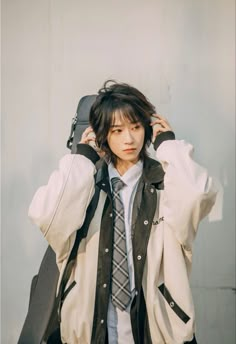 a young man wearing a jacket and tie with his hands on his head while standing in front of a white wall