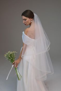 a woman in a white wedding dress holding a bouquet of flowers and wearing a veil