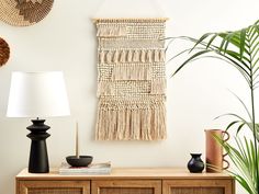 a wall hanging on the side of a wooden cabinet next to a lamp and potted plant