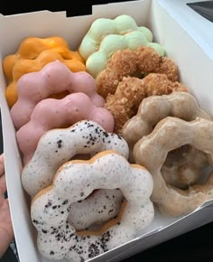 a box filled with different flavored donuts on top of a table next to a person's hand