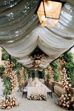 an outdoor dining area with tables and chairs covered in white drapes, flowers and greenery