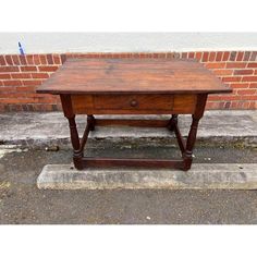 an old wooden table sitting in front of a brick wall on the side of a street