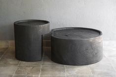 two round concrete tables sitting next to each other on a tile floor in front of a wall