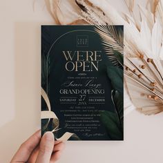 a person holding up a black and white wedding card with gold foil lettering on it